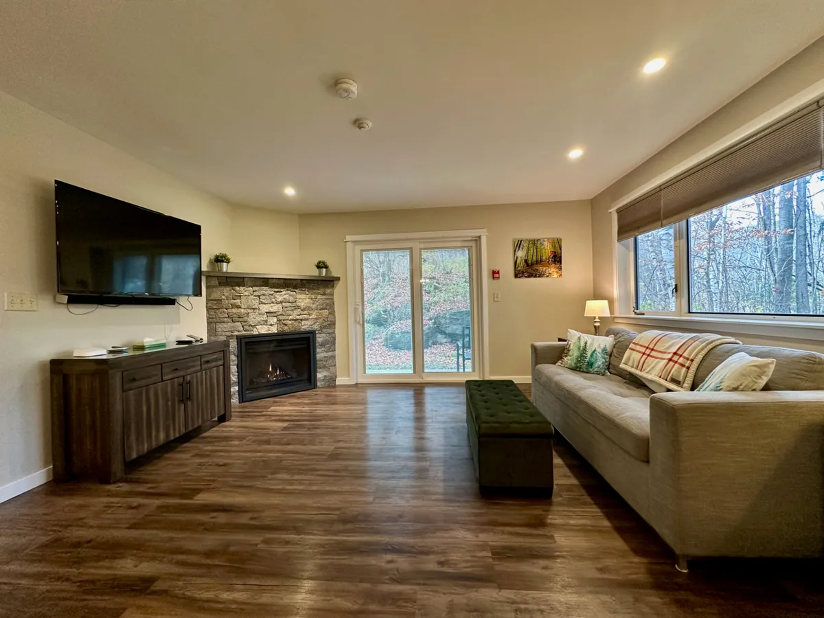 A cozy living area featuring a contemporary fireplace, comfortable sofa, and large window bathed in warm light. The window provides a glimpse of the outdoors, reinforcing the connection between adventure and relaxation.