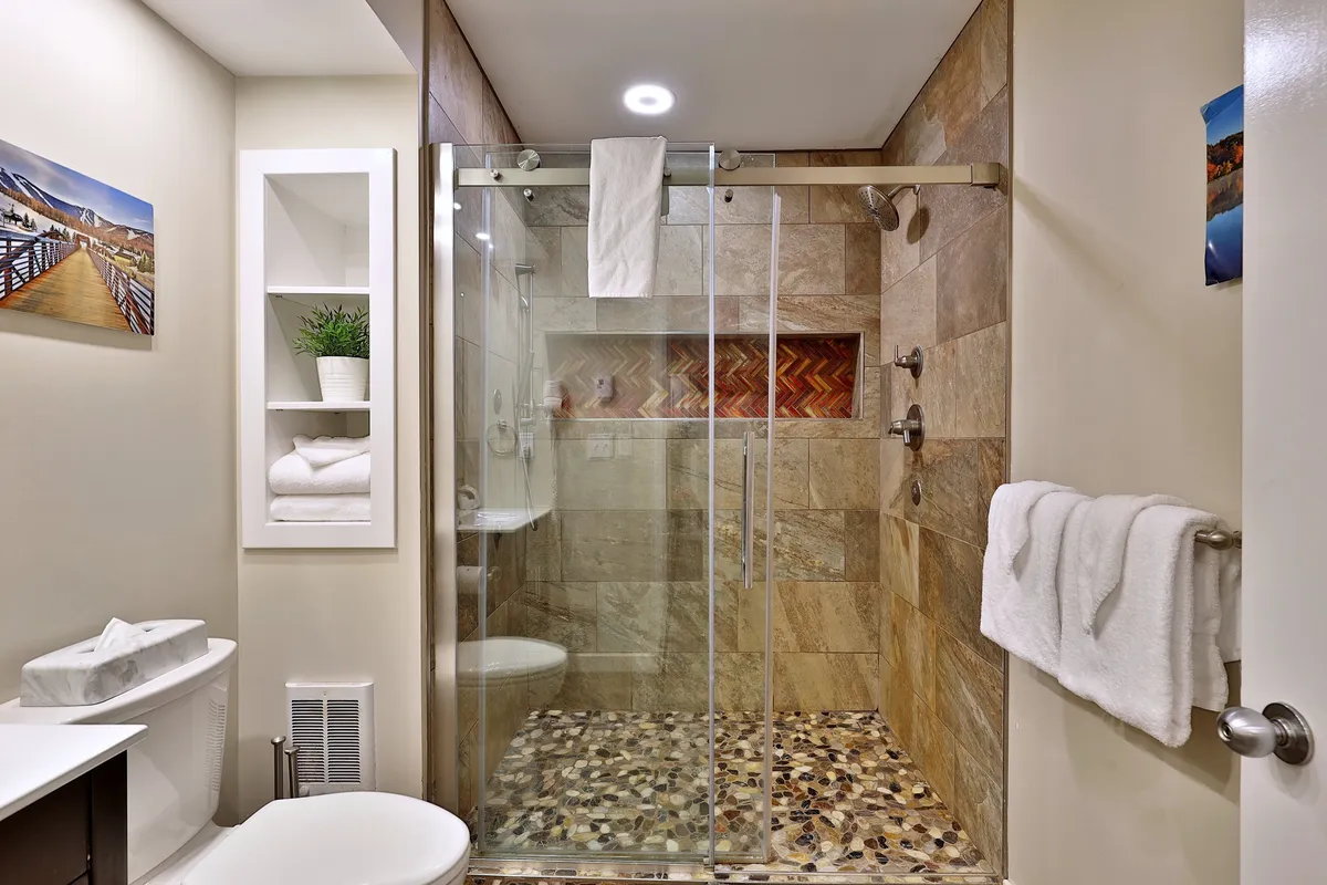 A modern bathroom with a striking glass shower enclosure, textured tile wall, and decorative art piece. The space feels fresh, clean, and inviting, emphasizing contemporary finishes and relaxation.