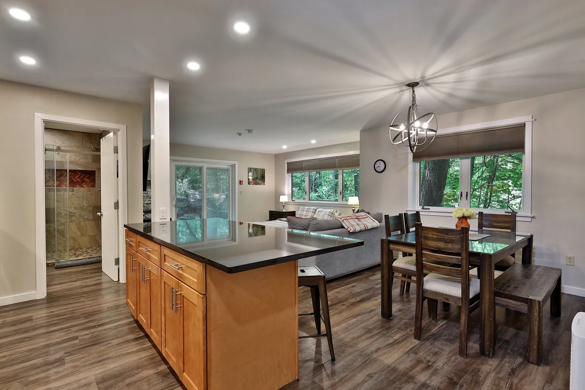 This image captures an open-plan living space featuring a kitchen island, a dining table, and a cozy living area with a sofa. The room has a welcoming atmosphere, ideal for socializing, relaxing, and sharing meals. Natural light fills the space, highlighting its warm, comfortable design.