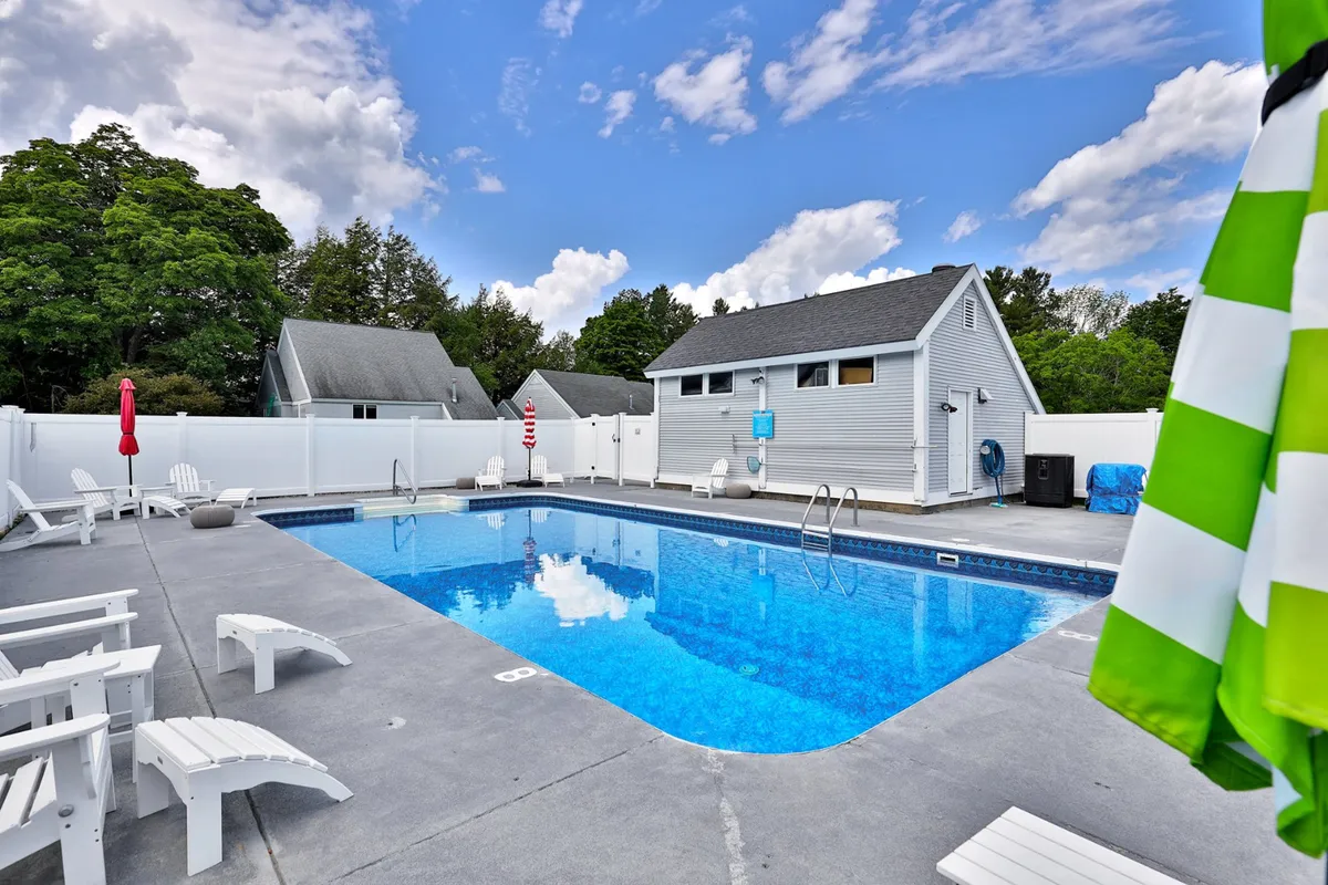 This exterior image centers on a sparkling outdoor swimming pool surrounded by lounge chairs, a green and white striped umbrella, and trees providing a lush, inviting backdrop. The space is clearly designed for leisure and social gatherings, evoking a resort-like atmosphere that invites both activity and relaxation.