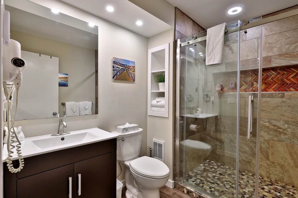 A bright, modern bathroom featuring a sleek vanity, a glass shower, and tasteful decorative artwork. The space is immaculate and thoughtfully arranged, suggesting spa-like comfort and attention to guest well-being.