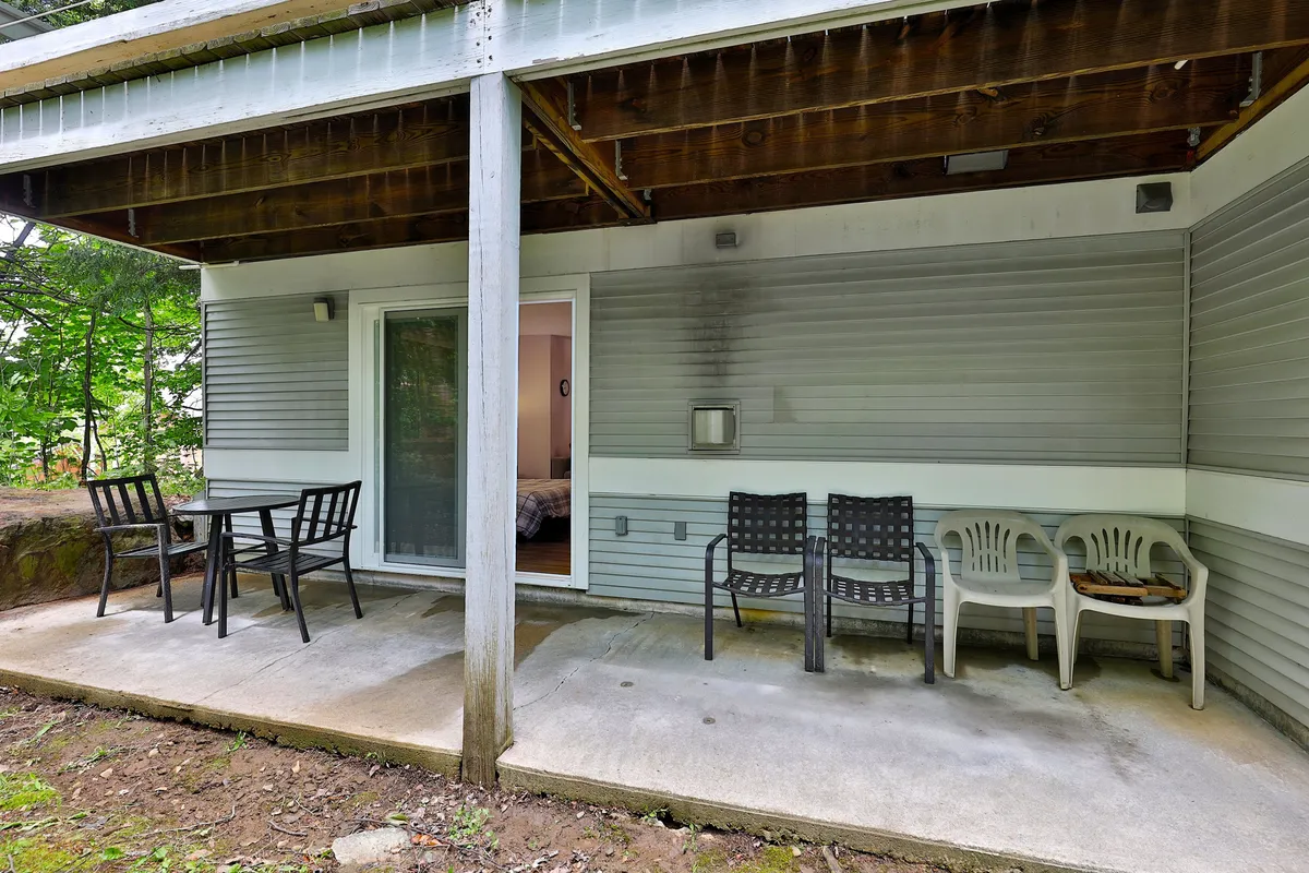 The outdoor patio features comfortable furniture, a sliding glass door, and is surrounded by lush greenery. This space seamlessly connects the indoors to the outside, offering a spot for morning coffee or evening relaxation.