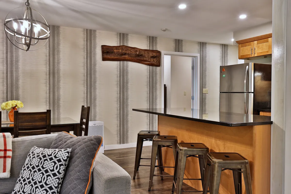 A modern kitchen and dining space anchored by a kitchen island and chandelier. The scene includes a comfortable dining table and a textured accent wall, all set in a welcoming atmosphere suited for small gatherings or romantic meals.