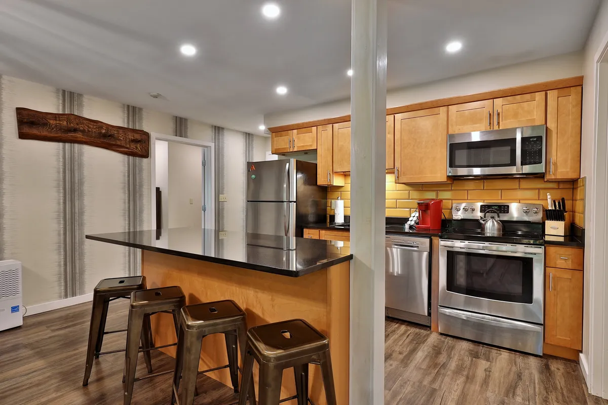 A close perspective on the modern kitchen, highlighting the kitchen island with seating, stainless steel appliances, and warm wooden cabinetry. The setup suggests both everyday ease and special group cooking experiences.