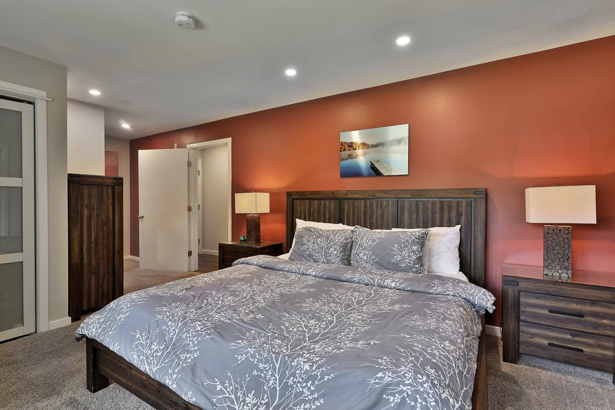 A calm, serene king bedroom featuring a plush bed with patterned bedding, wooden nightstands, a decorative lamp, and wall art. The space is bathed in natural light, creating a peaceful atmosphere perfect for relaxation or restorative sleep.