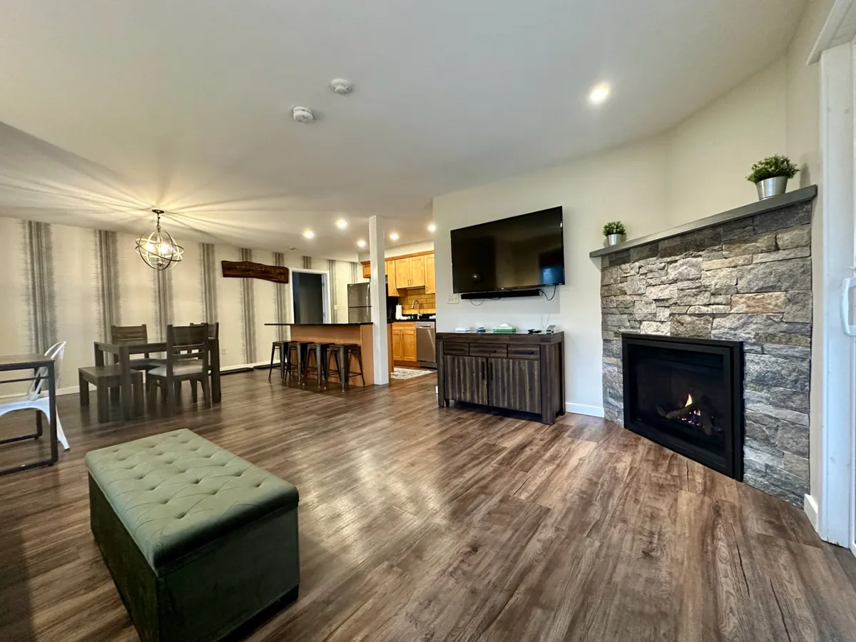 This cozy interior scene features a warm fireplace, a dining table, comfortable seating, and a television. The setting is perfect for family gatherings or intimate evenings, suggesting comfort and relaxation during the colder months.
